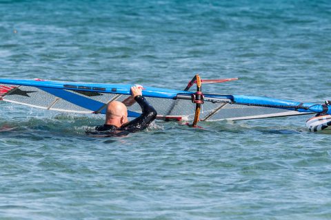 Now that the sail has lifted and you have seen and felt that all the water is off the leach of the sail you can continue to draw the mast up, across and over your head. Continue to gently kick your legs so you are still swimming upwind.