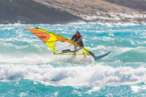 Begin to change your rails from heelside to toeside, carving upwind to carving downwind, into your top turn. Move your body over the board almost like you are trying to fall forwards head first. The head leads your weight change and it also begins to look downwind to where you want to go.