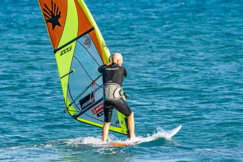 Reach under and collect the new side of the boom with an overhand grip and send the rig forward to help keep you across the wind and to flatten the board.