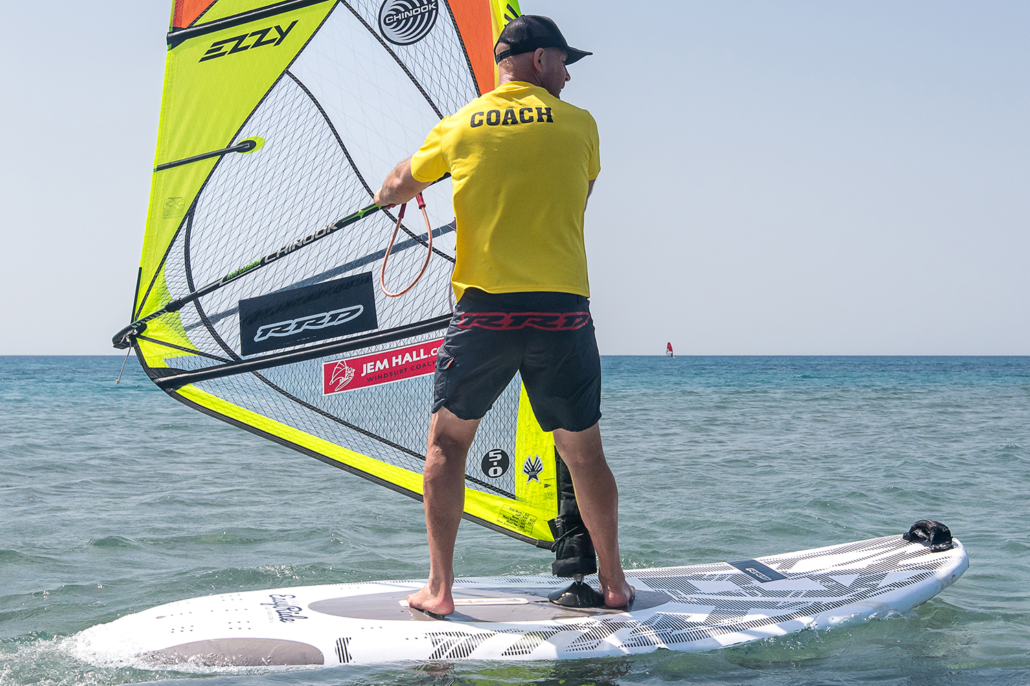 Set up across the wind. Place your front hand on the mast, or at the front of the boom, and put your foot on the mastfoot.