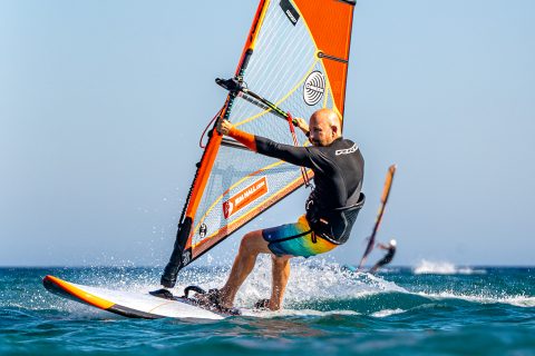 Look forward whilst planing in the straps, across the wind, place hand on mast, in readiness to unhook. Pull down on mast hand, and weight front foot to keep the board flat.