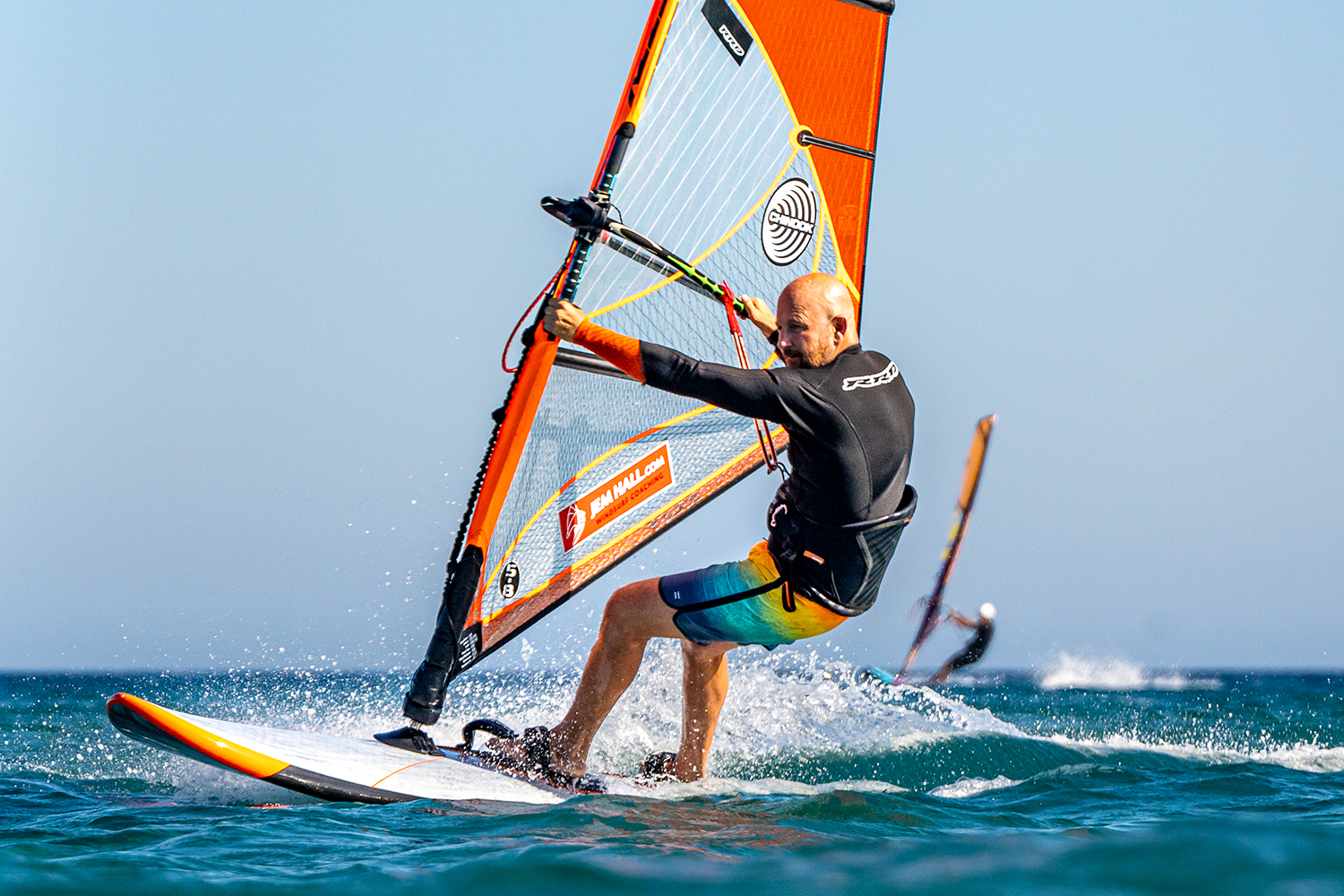 Look forward whilst planing in the straps, across the wind, place hand on mast, in readiness to unhook. Pull down on mast hand, and weight front foot to keep the board flat.